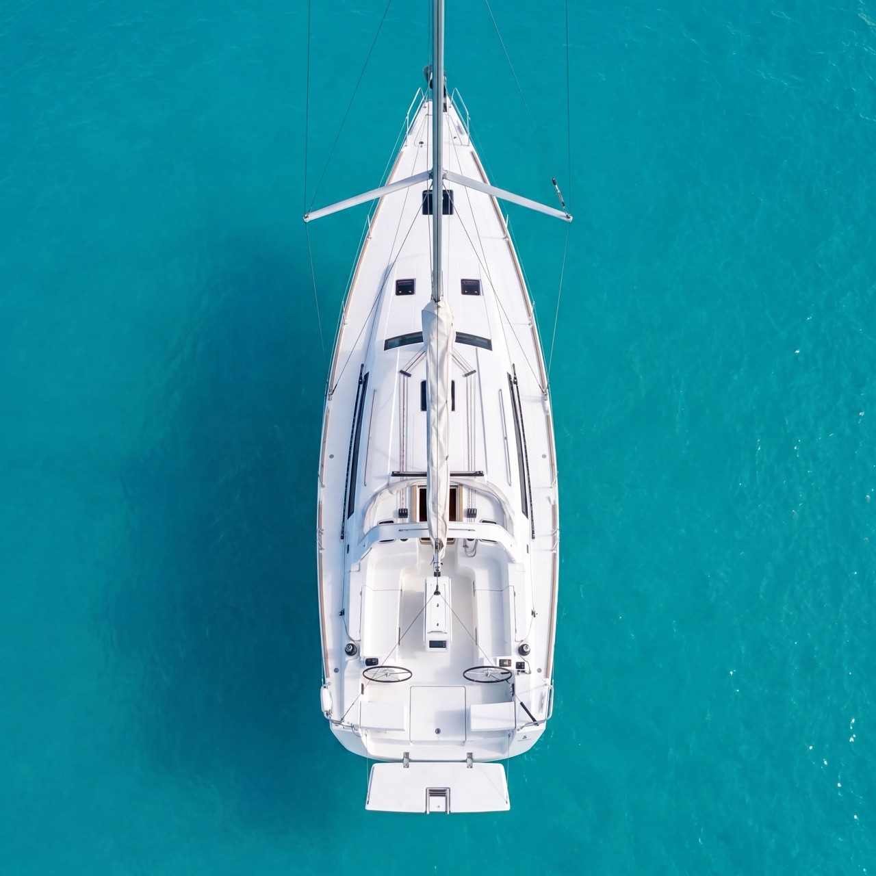 Aerial view looking straight down on a Beneteau Oceanis 45 sailing yacht anchored in turquoise water, showing its wide stern, twin helm wheels, and open cockpit.