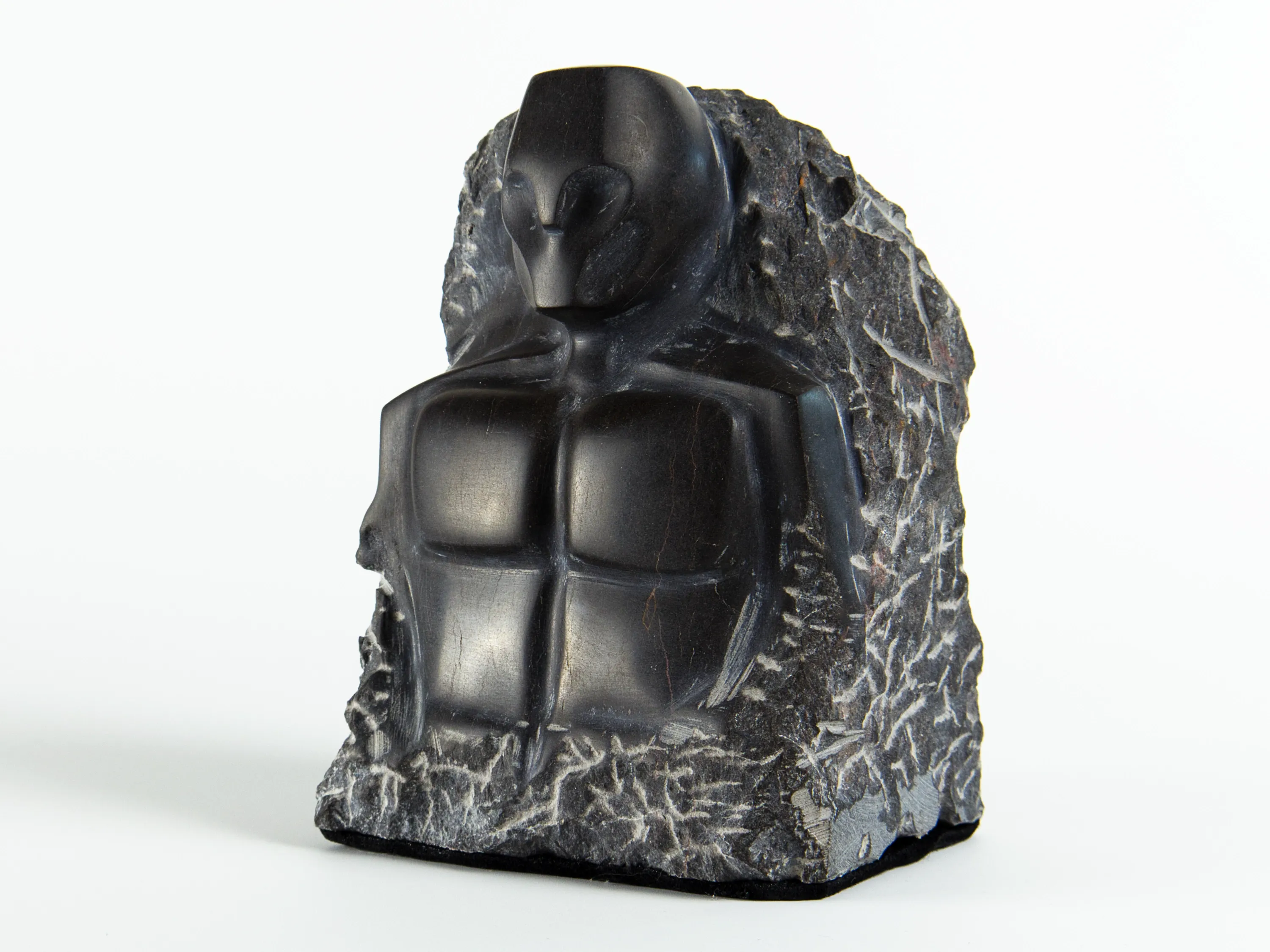 Handgemeißelte dunkle Steinskulptur Wächter des Abgrunds mit kantigem Torso und maskenartigem Gesicht vor rauem Naturstein
