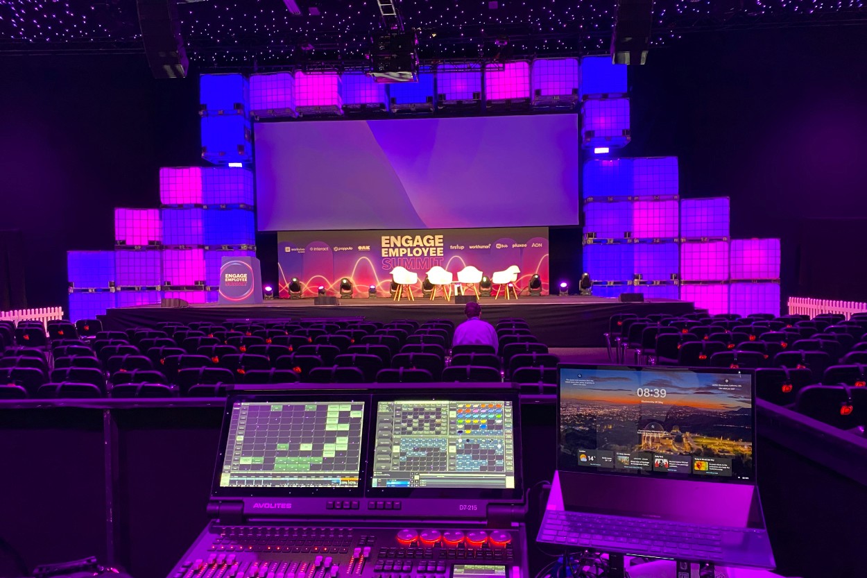 The Engage Employee Summit main stage before doors open, shot from the lighting desk, with panel chairs set and sponsor branding across the backdrop.