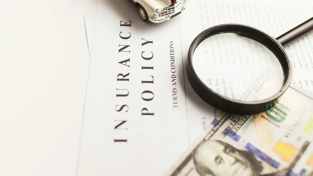 Insurance policy document with a magnifying glass, toy car and banknotes, illustrating liability, insurance cover and risk management in sports sponsorship agreements.
