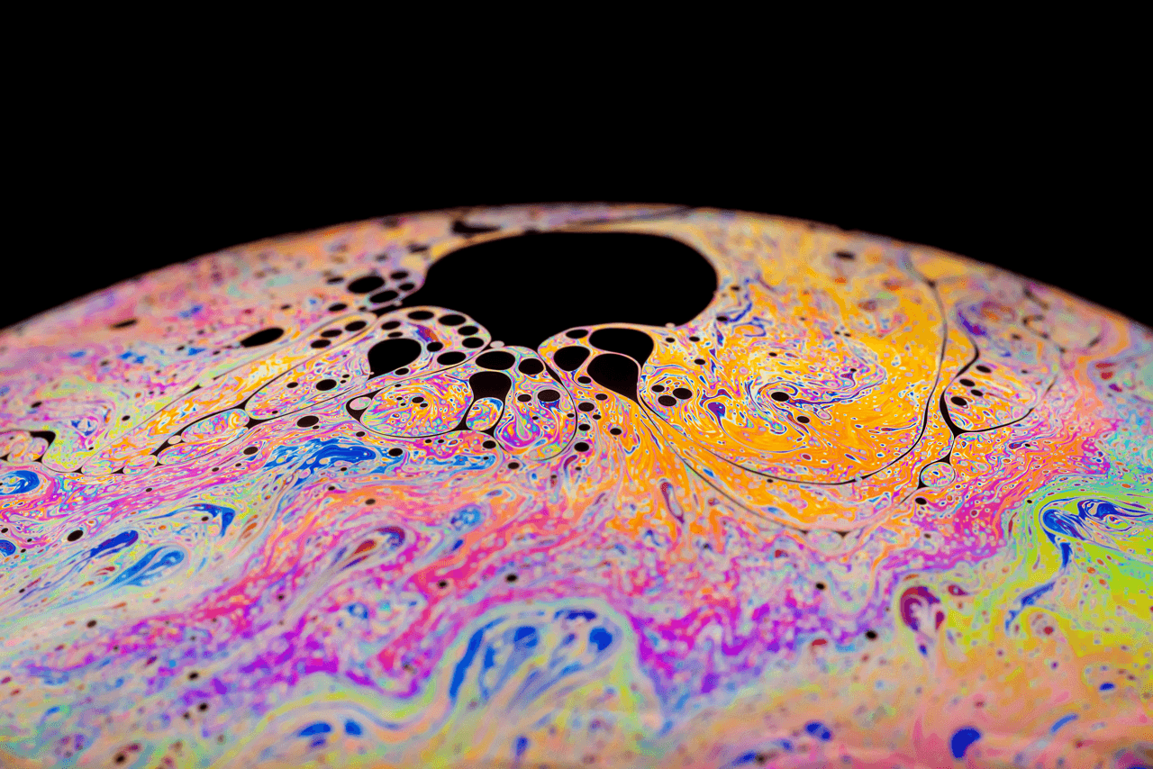 Abstraktes Seifenblasenmuster mit schillernden Farben und schwarzen Flecken.