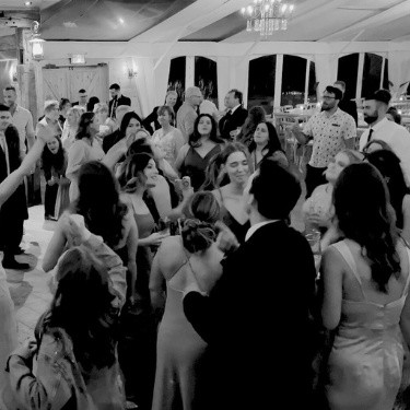 Guests joyfully dancing under a beautifully lit tent at an outdoor wedding, surrounded by a festive and lively atmosphere.