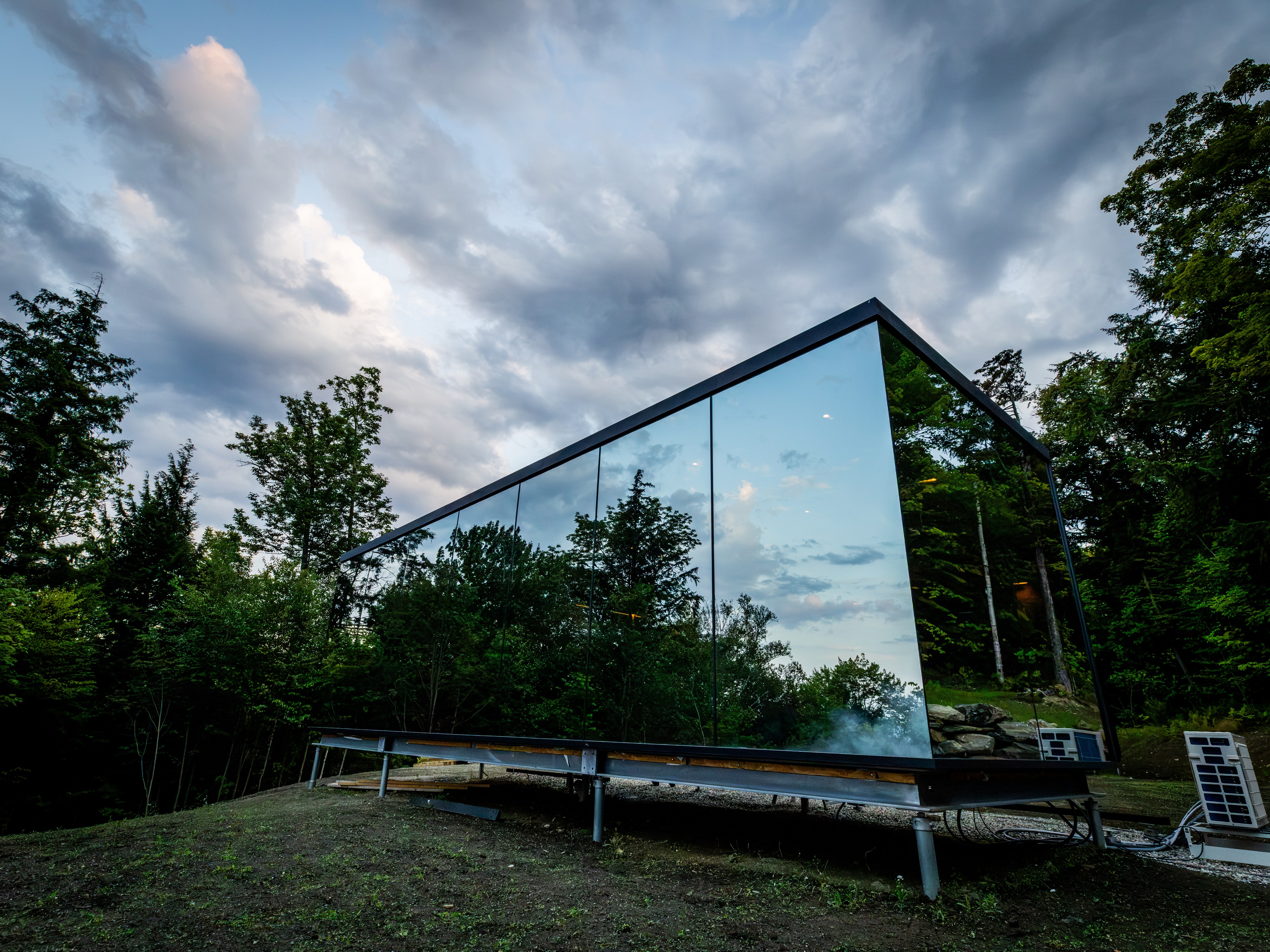 Side view of the mirrored cabin against the woods