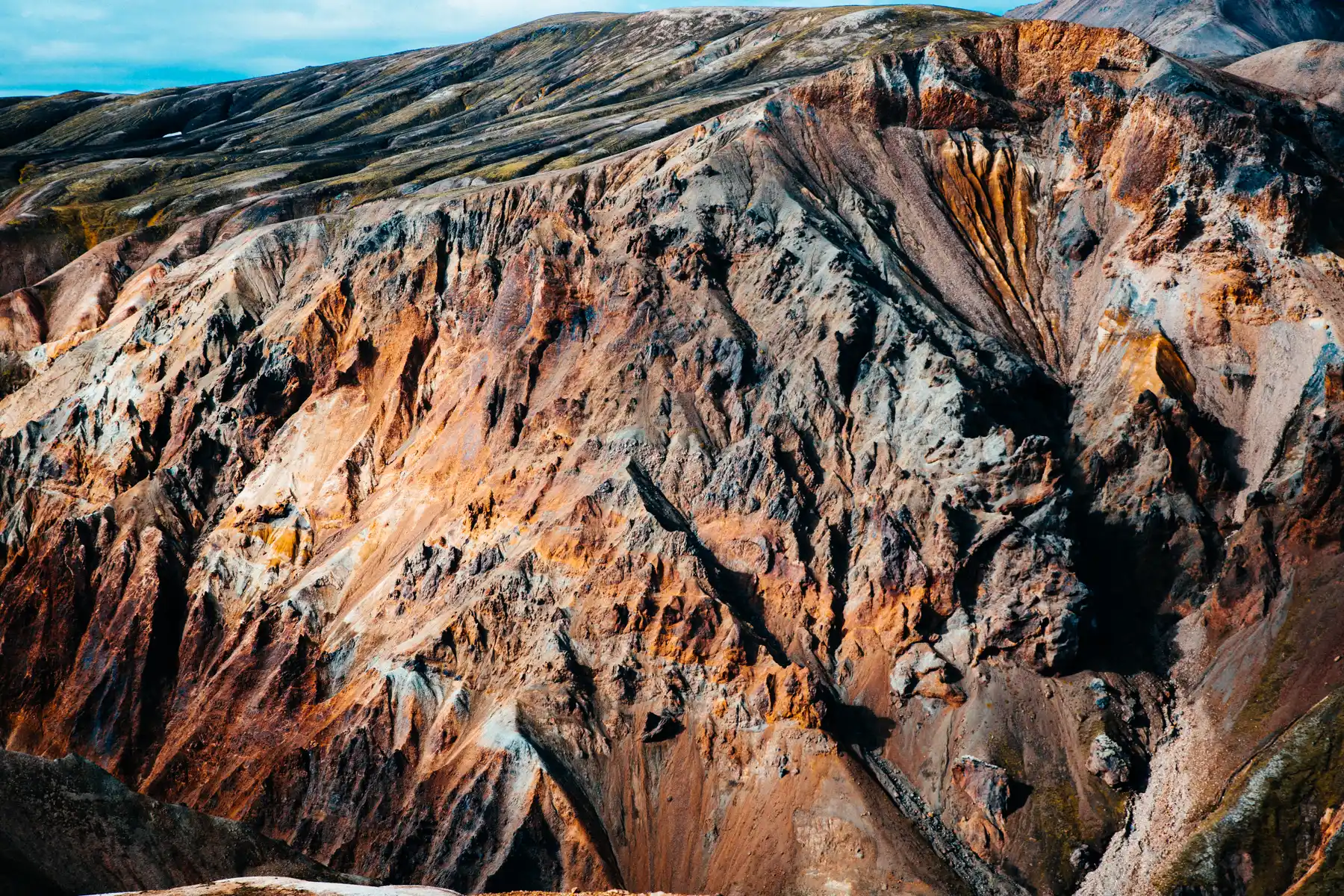 Aerial of a mineral-streaked mountainside in ochre, grey and black