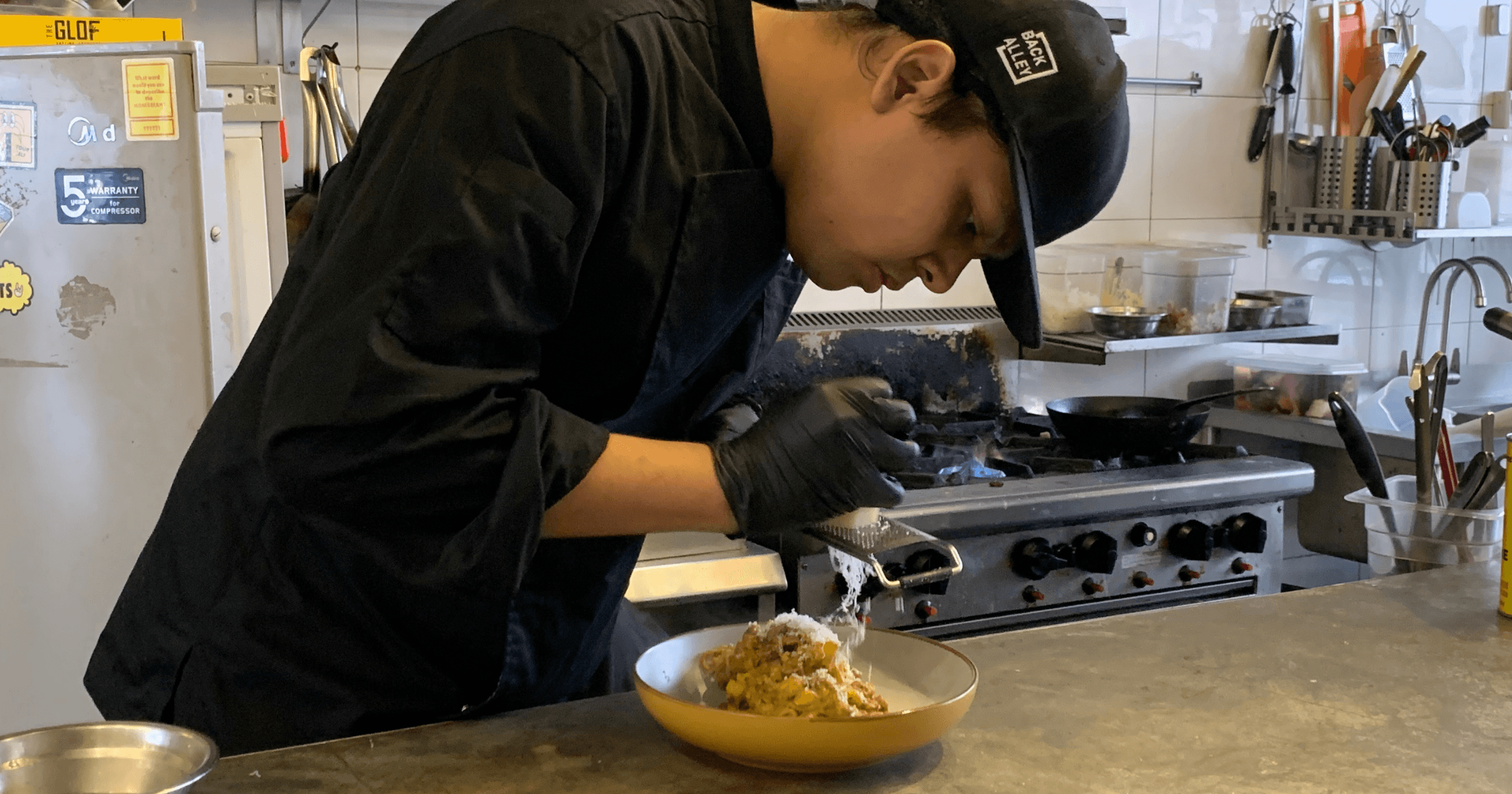 A Back Alley Pasta Bar staff shredding cheese on a pasta