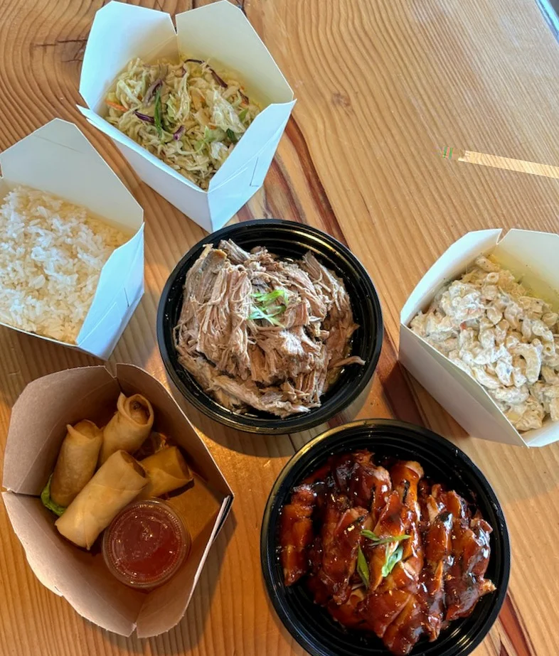 A top-down view of the Special Family Sized Mix Plate featuring Huli Huli chicken, Kalua pork, four spring rolls, rice, mac salad, and slaw in takeout containers.
