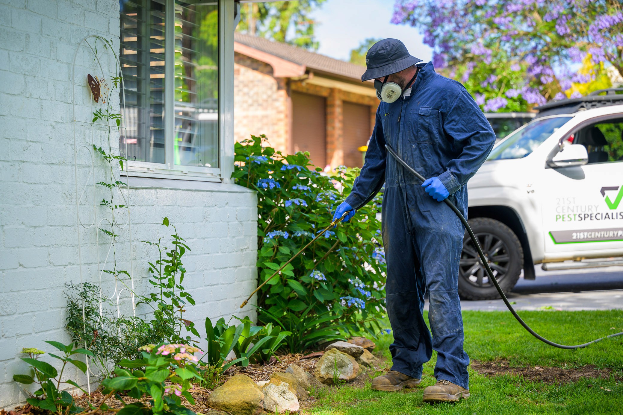 Pest technician doing periiter spray in garden outside house
