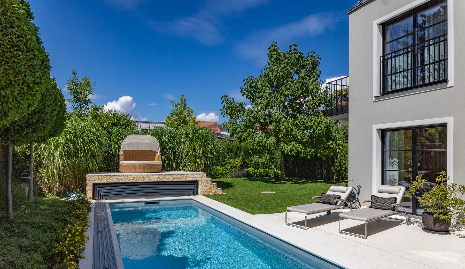 Familiengarten mit Pool, Rasenfläche und erhöhter Terrasse am Wohnhaus.