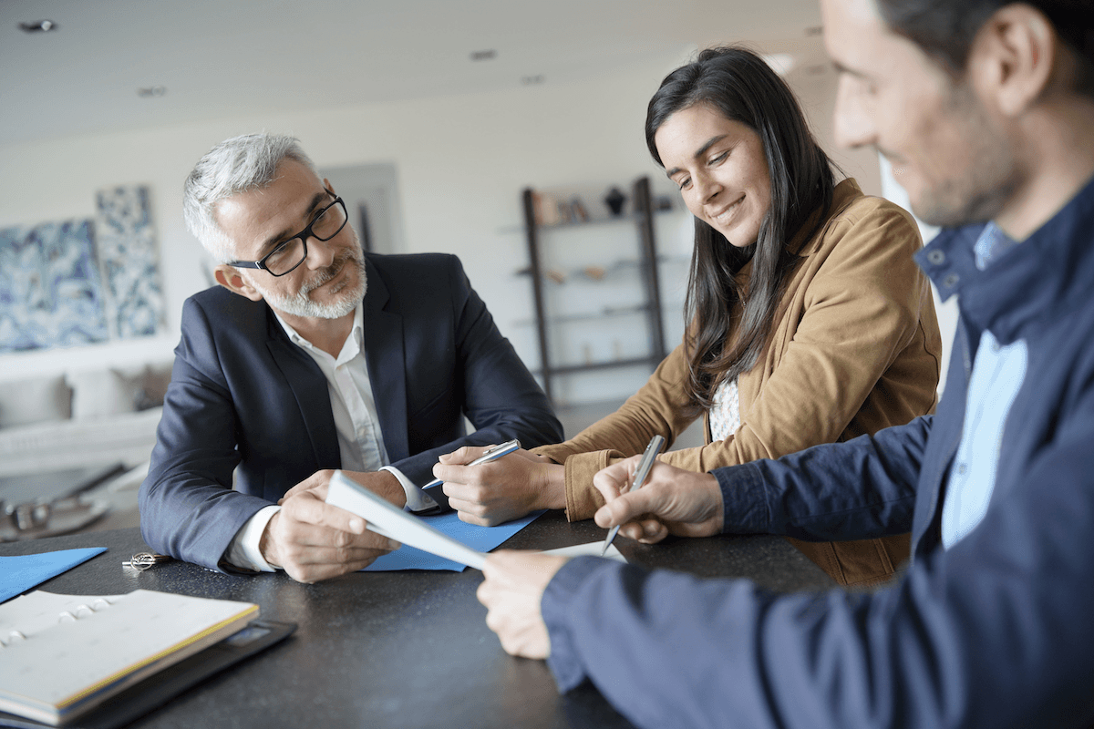 man signing a document in front of two other people