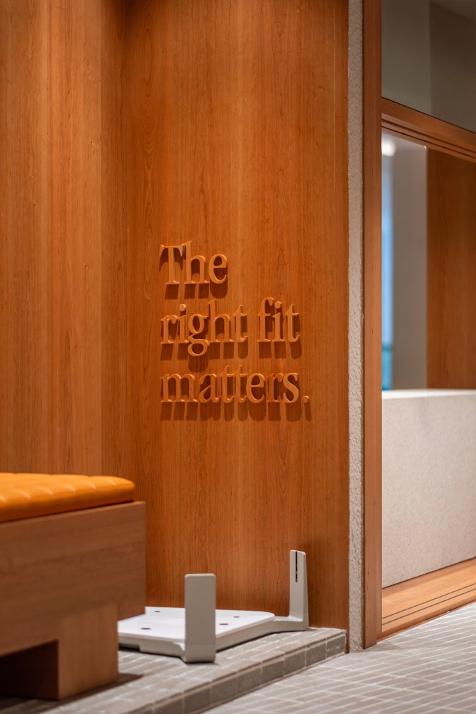 Interior of a New Balance Run Hub showcasing a wooden wall with the phrase 'The right fit matters.' carved in relief, alongside a bench and flooring details.