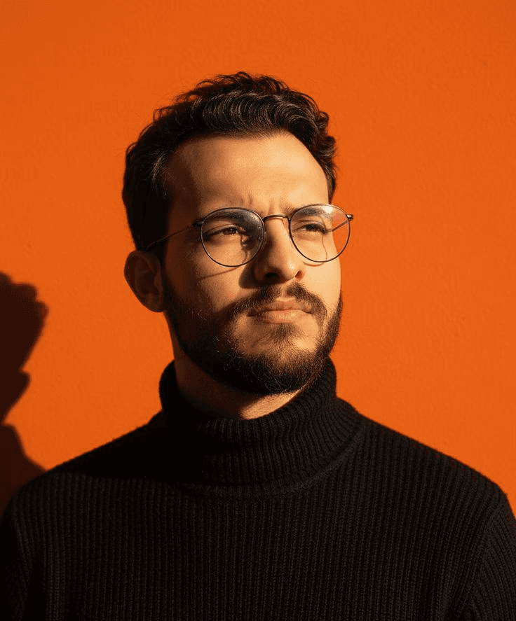 A man with glasses and a beard looks thoughtfully into the distance. He's wearing a black turtleneck against a vibrant orange background, conveying a modern and contemplative tone.