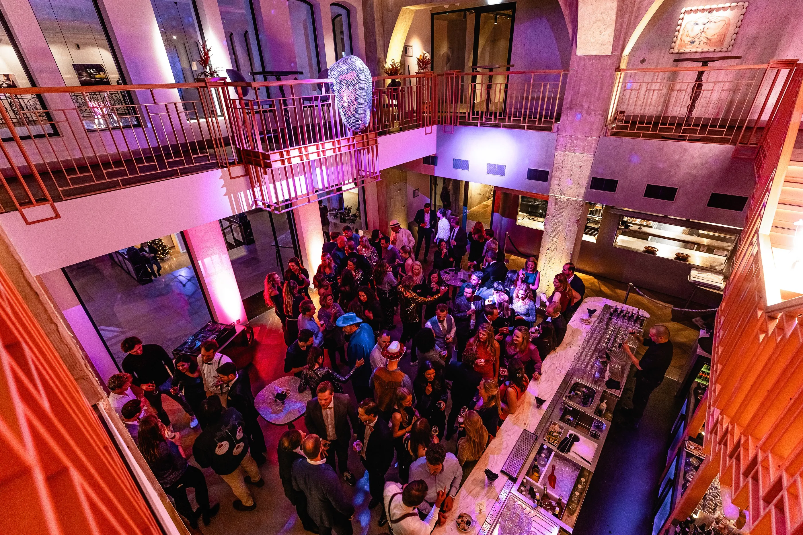 A view of a crowded event space with colorful lighting and people mingling below.