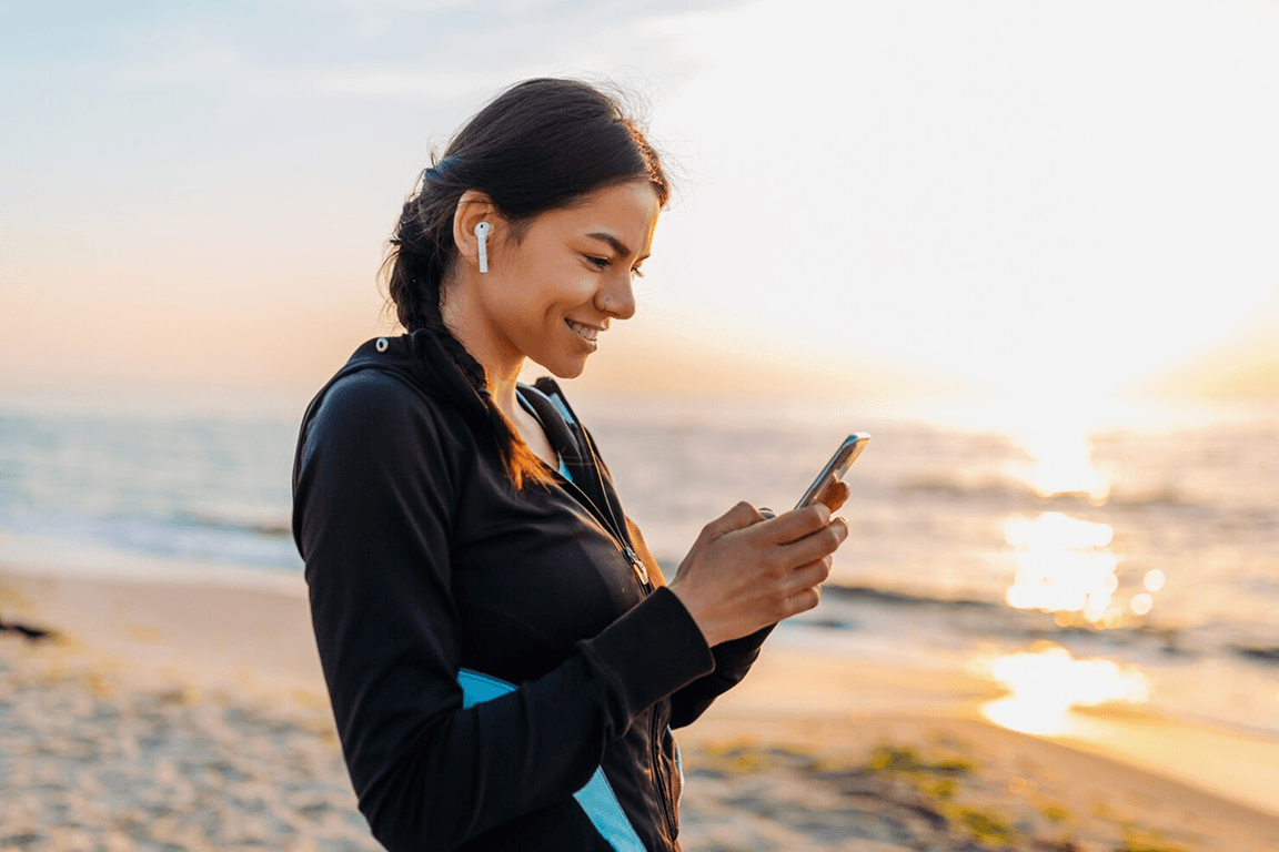 Woman using a mobile health app on her smartphone outdoors at sunset, representing the benefits and features of mobile health apps in 2026.