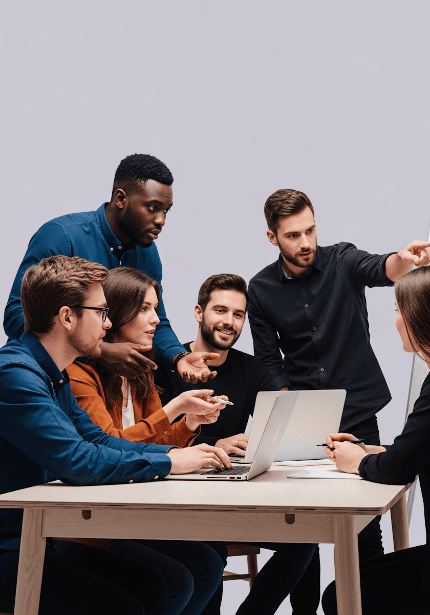 Diverse team of professionals collaborates around a table with laptops; one man points while they discuss ideas.