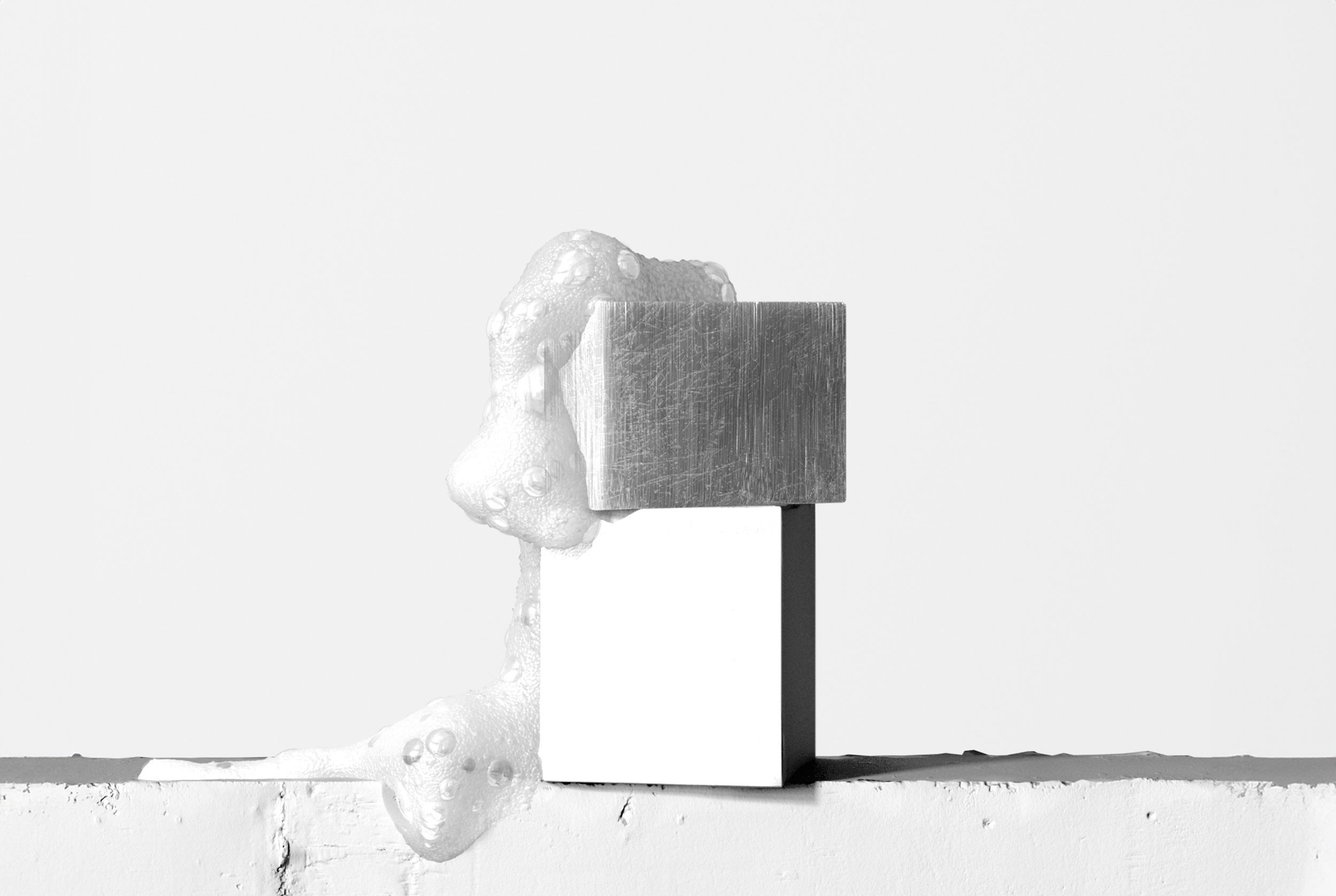 A black and white photo of two stacked metal blocks with foam oozing between them.