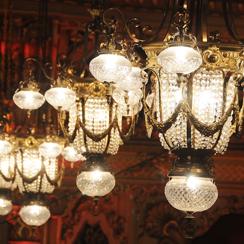 Several ornate crystal chandeliers with glowing lights, hanging from a decorative wooden ceiling.
