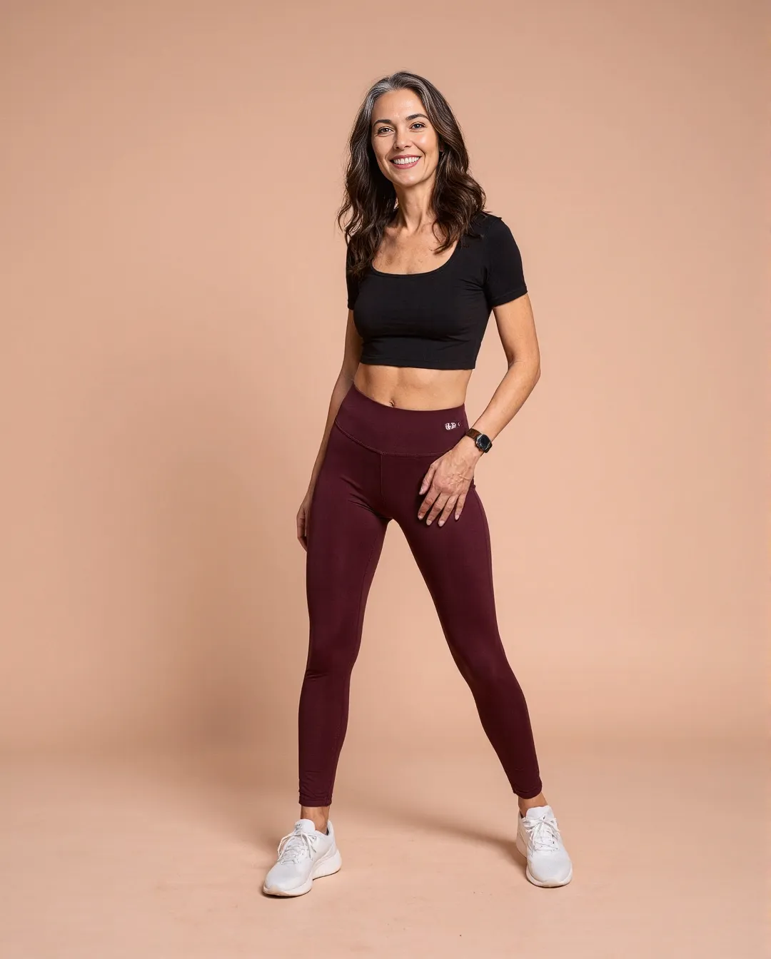Professional athleisure photography featuring burgundy leggings and black crop top against warm beige backdrop, showcasing fitness apparel