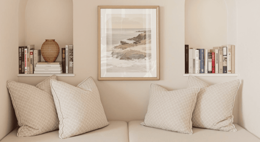 Cozy arched nook with beige cushions, pillows, books, and coastal artwork.