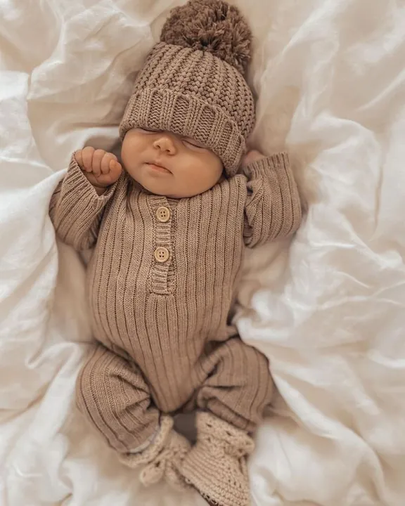 Sleeping baby in a brown knit outfit, pompom hat and tiny booties
