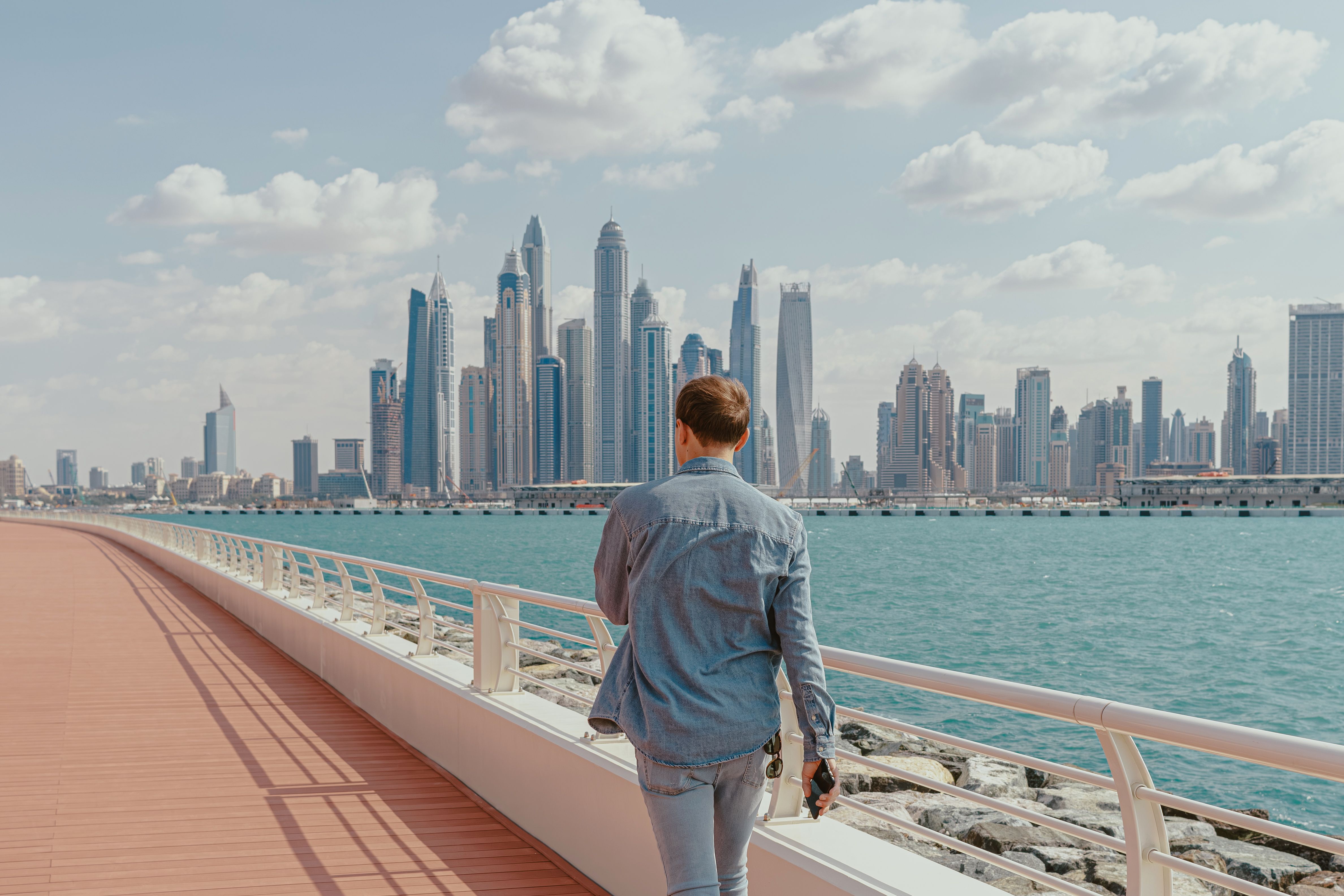 back-view-of-a-man-walking-along-a-waterfront-promenade-with-dubai-marina-skylin - kate-trysh (pexels)