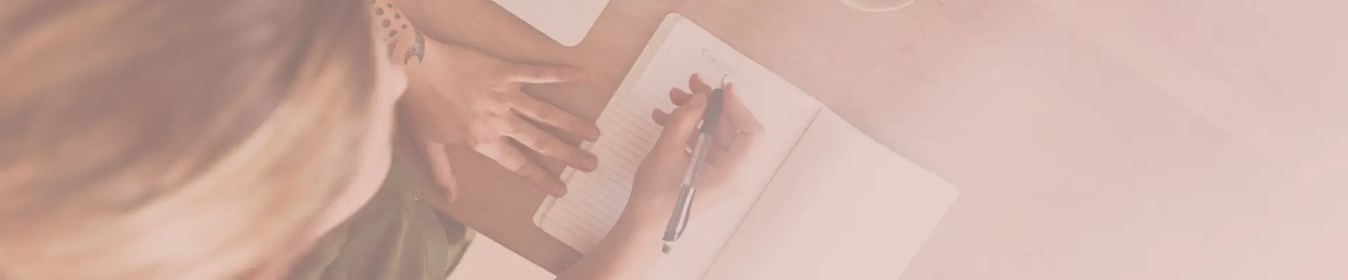 Top view of a person writing in a wishlist notebook at a desk, symbolizing intentional planning before online shopping.