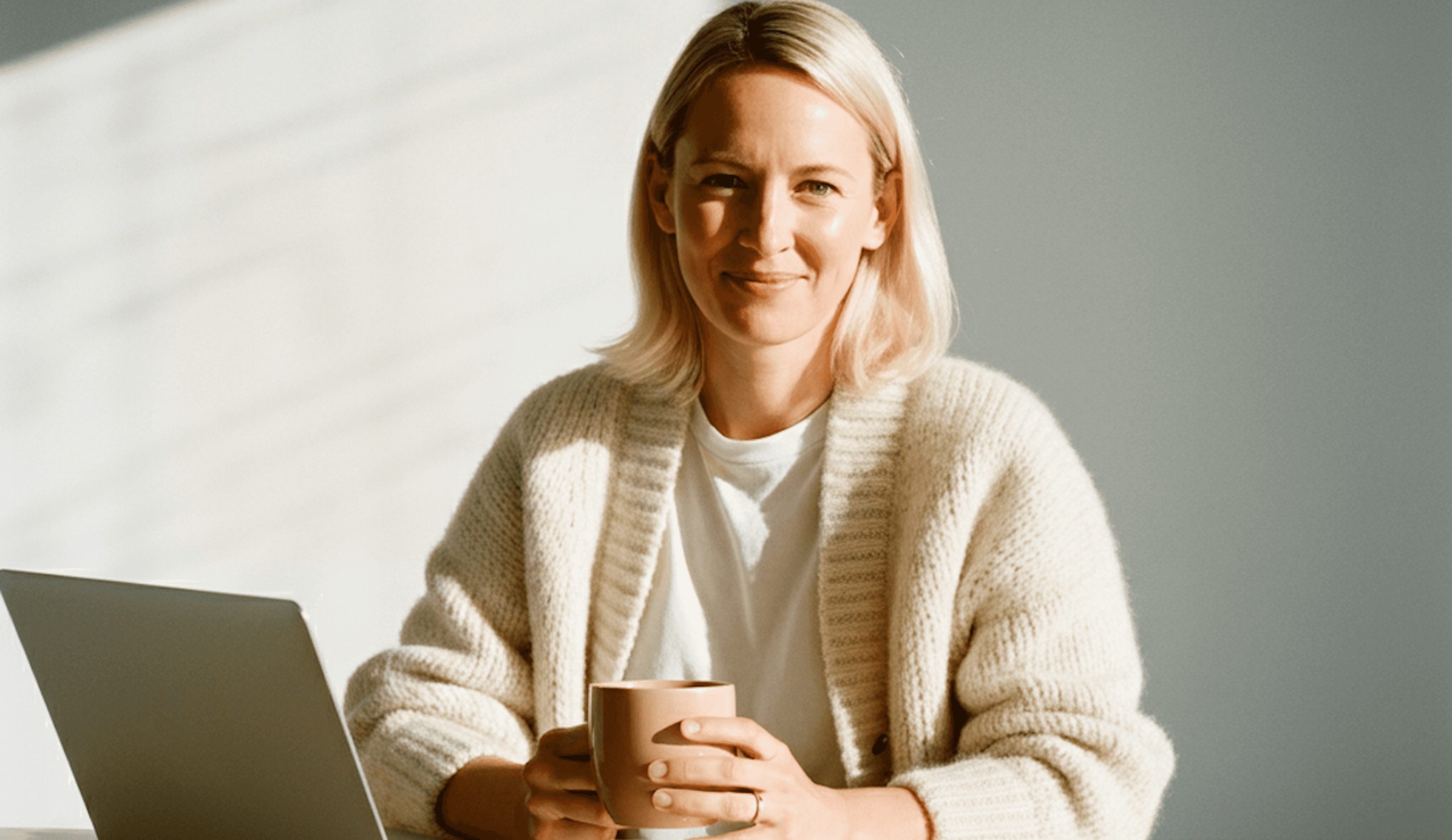 Confident female professional using a laptop at a bright workspace with a coffee cup