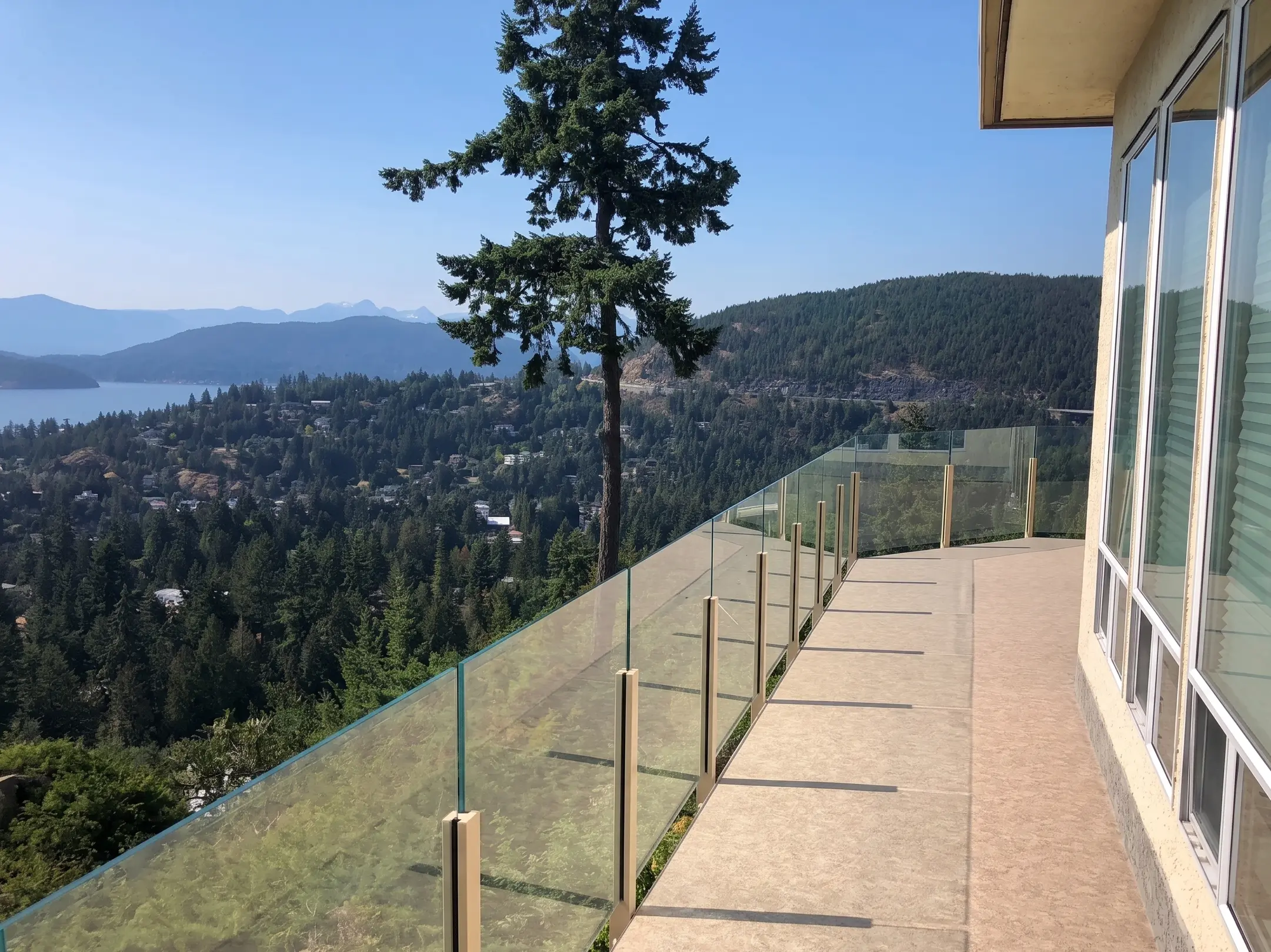 Frameless glass railing on a long oceanfront deck with panoramic views of the coastline and forested mountains