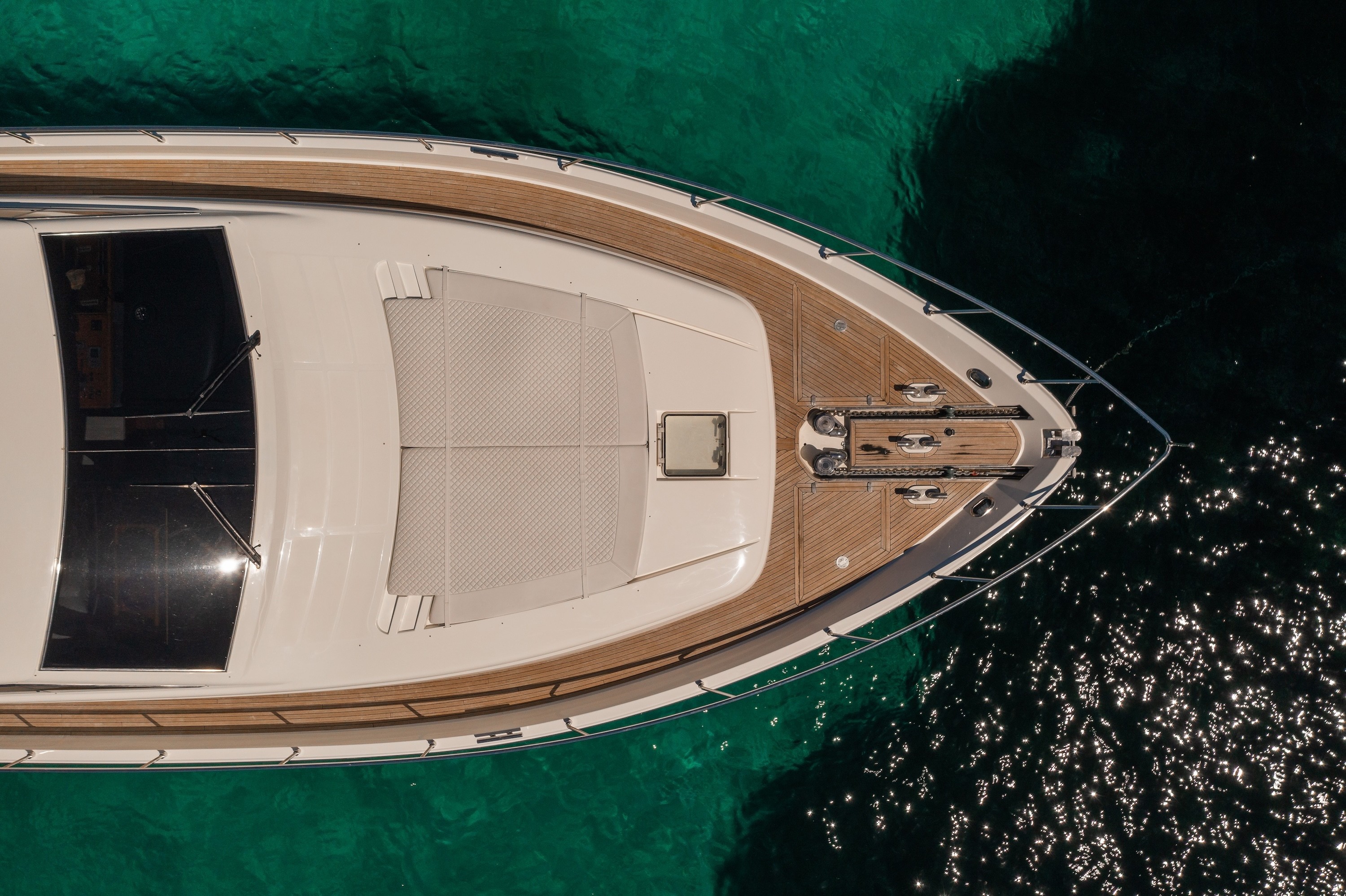 Aerial view of luxury Ferretti 68 yacht's bow deck with teak trim floating in crystal-clear emerald waters.