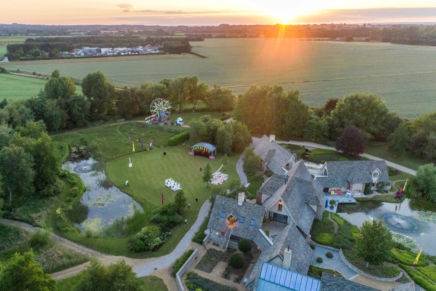 An aerial view of a countryside estate with stone buildings, greenery, and a vibrant sunset.