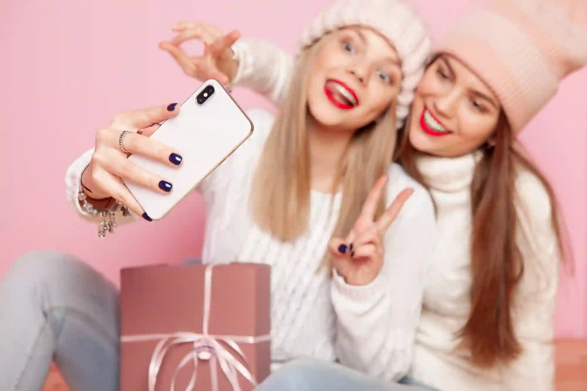 Two friends in winter hats taking a selfie with a gift box.