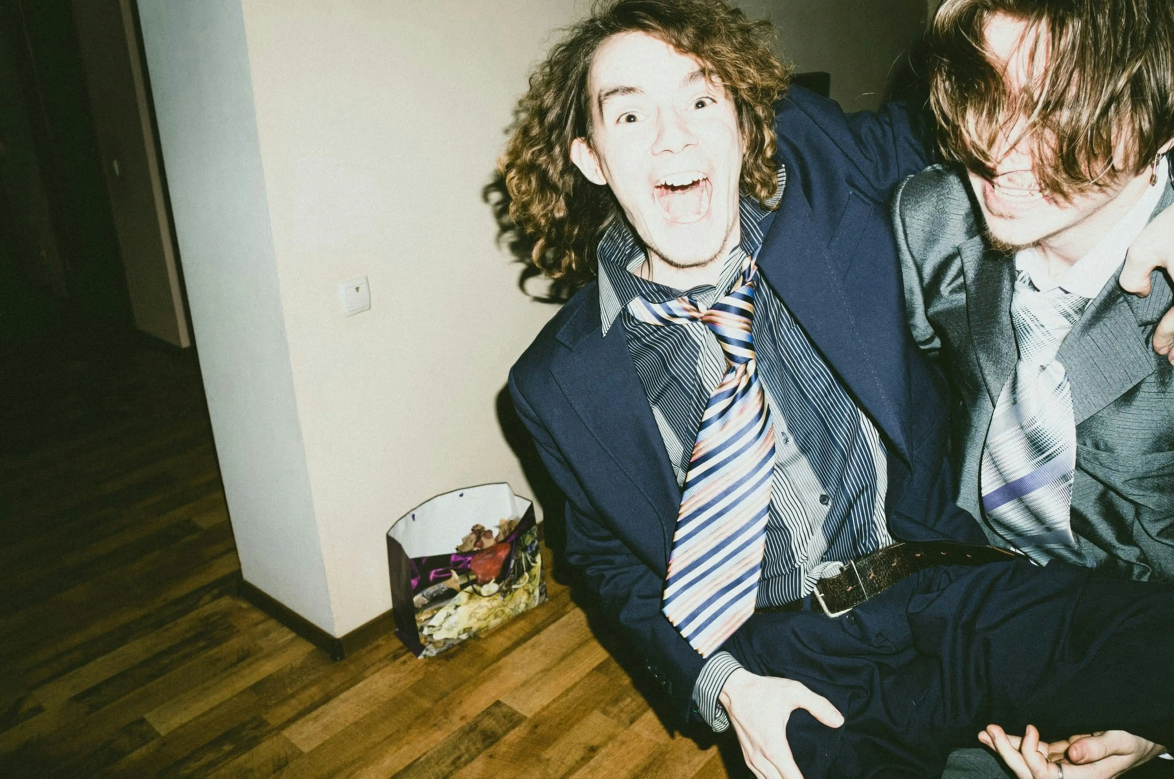 Two people laughing and hugging while dressed in suits and ties, captured in a candid, high-energy indoor setting.