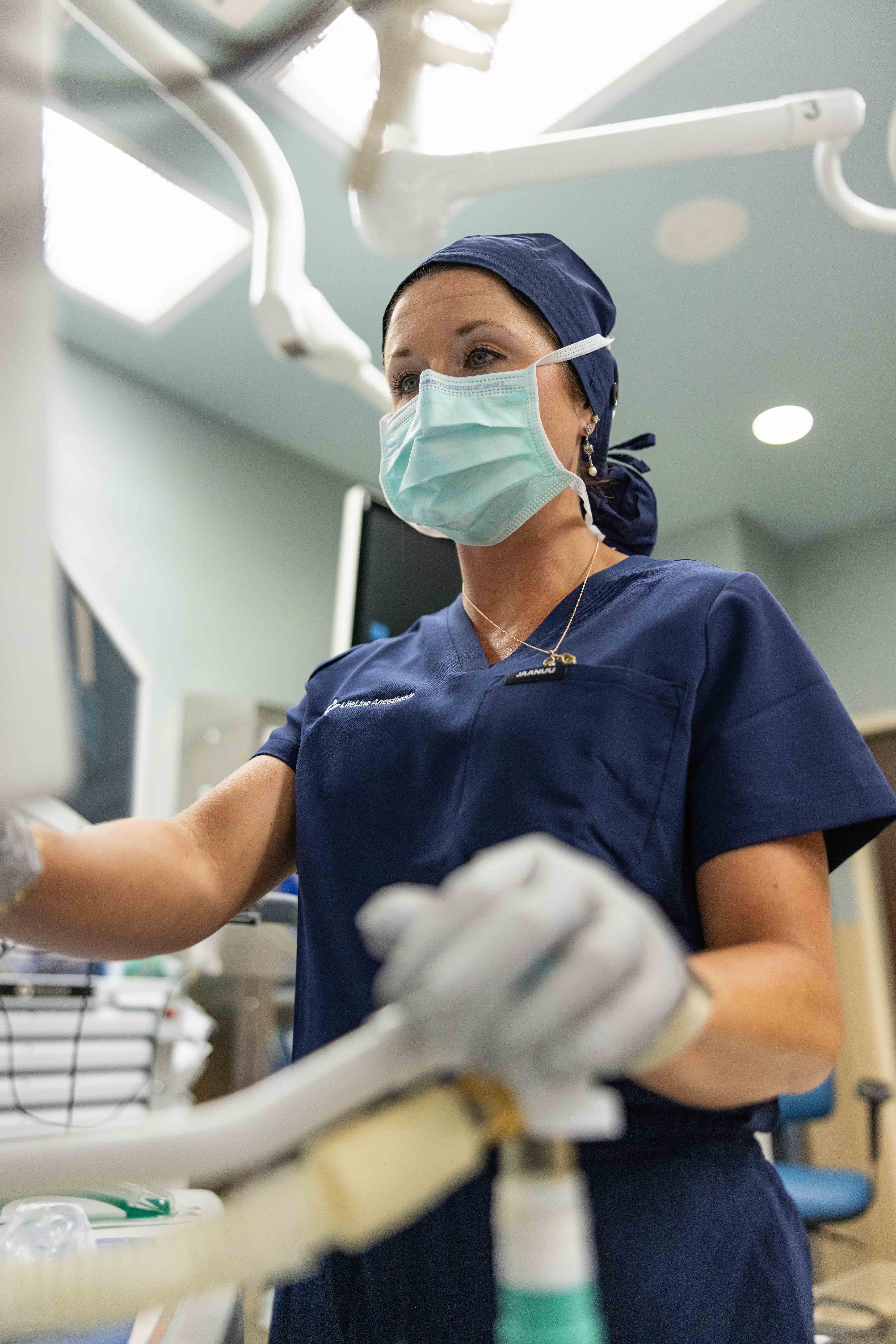A CRNA in scrubs and a surgical mask stands ready in an ASC procedure room, representing dependable anesthesia coverage and scheduling for ambulatory surgery centers