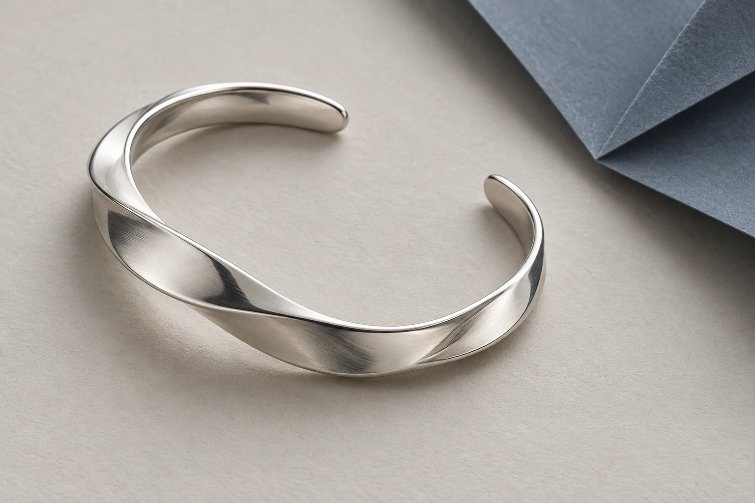 Separate fictional silver cuff on pale paper with a slate folded plane away from its open ends