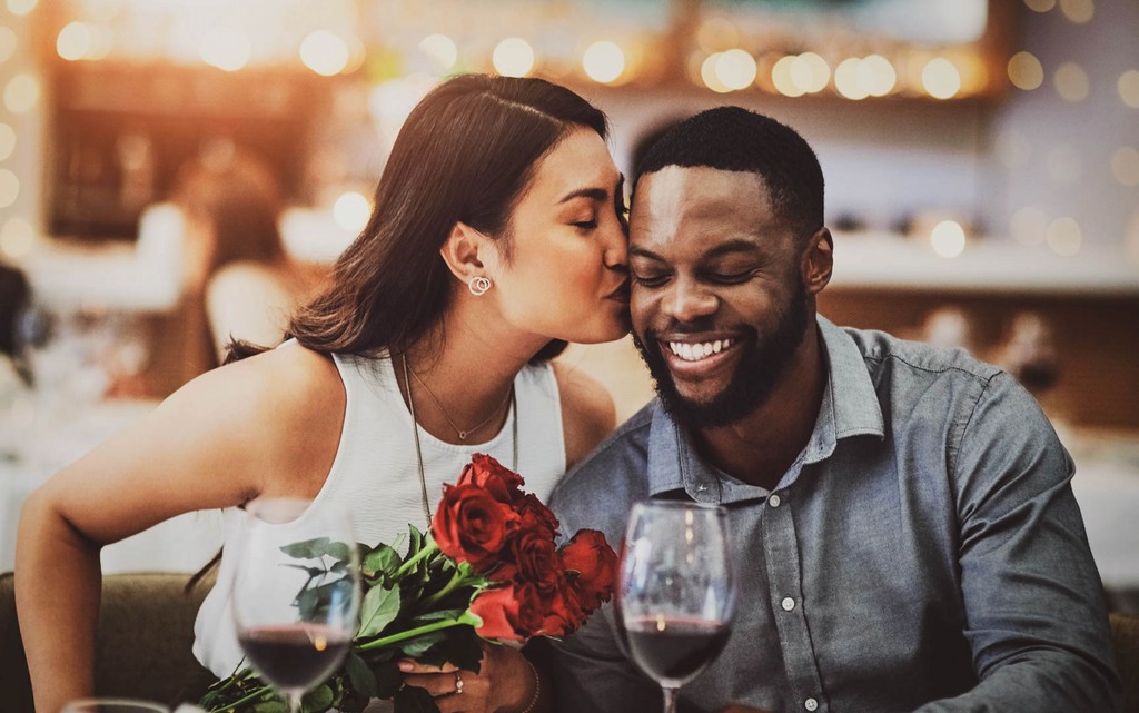 A woman with her eyes closed enjoys a delicious meal being fed to her by someone off-camera at a restaurant.