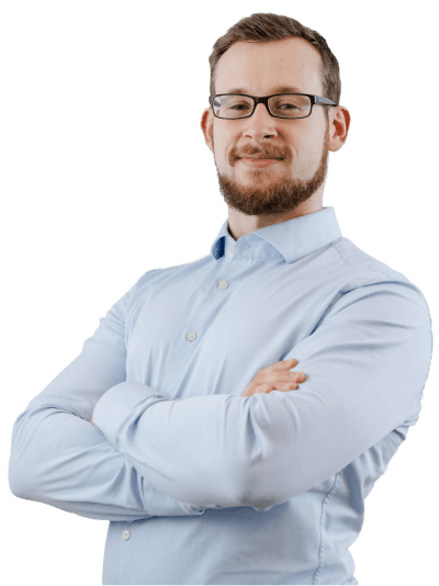 A confident individual with glasses and arms crossed, wearing a light blue shirt, stands against a neutral background.