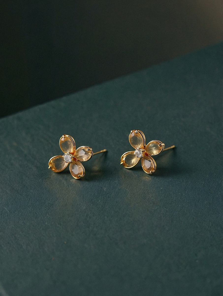 Elegant gold flower-shaped earrings with translucent petals and sparkling centers, displayed on a dark green textured surface.
