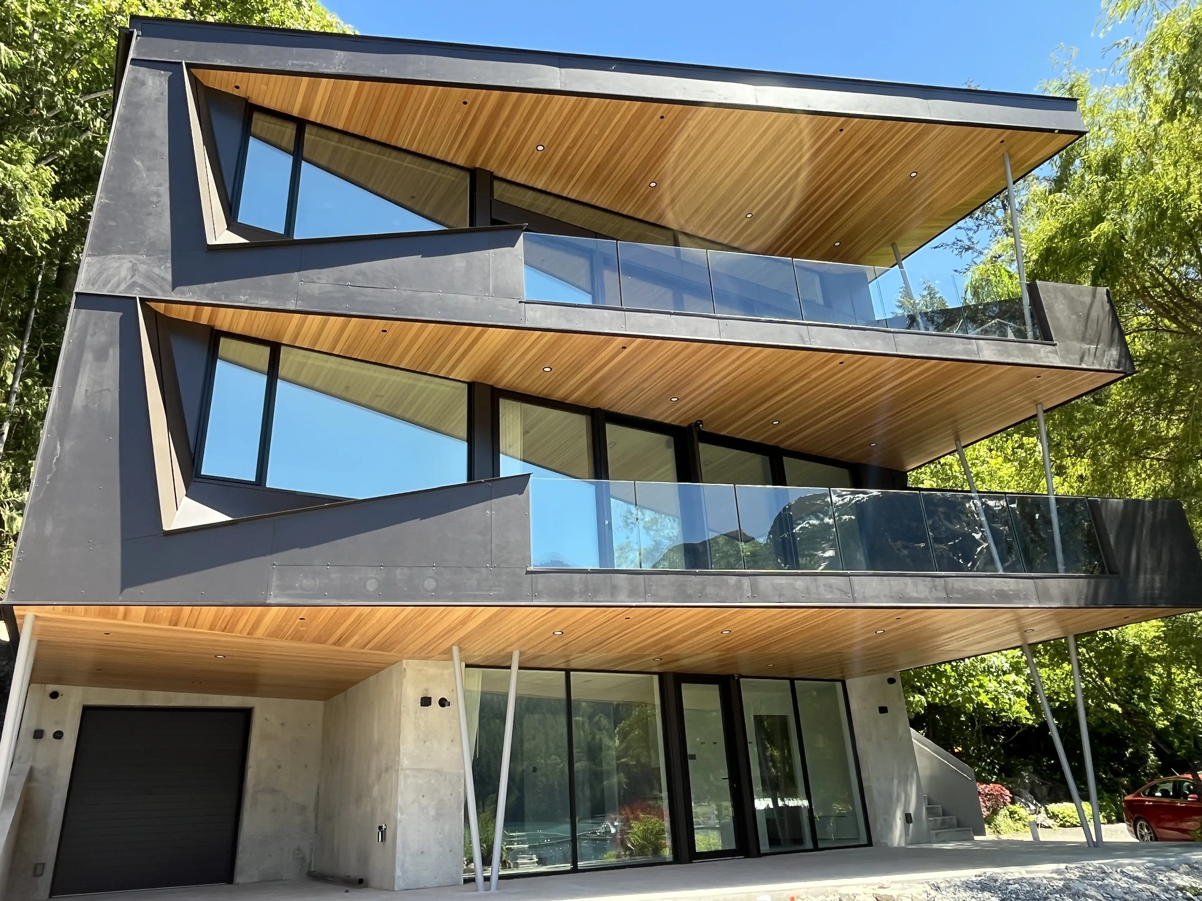 Frameless glass guardrails on the balconies of a modern multi-level home set against forest in coastal British Columbia.
