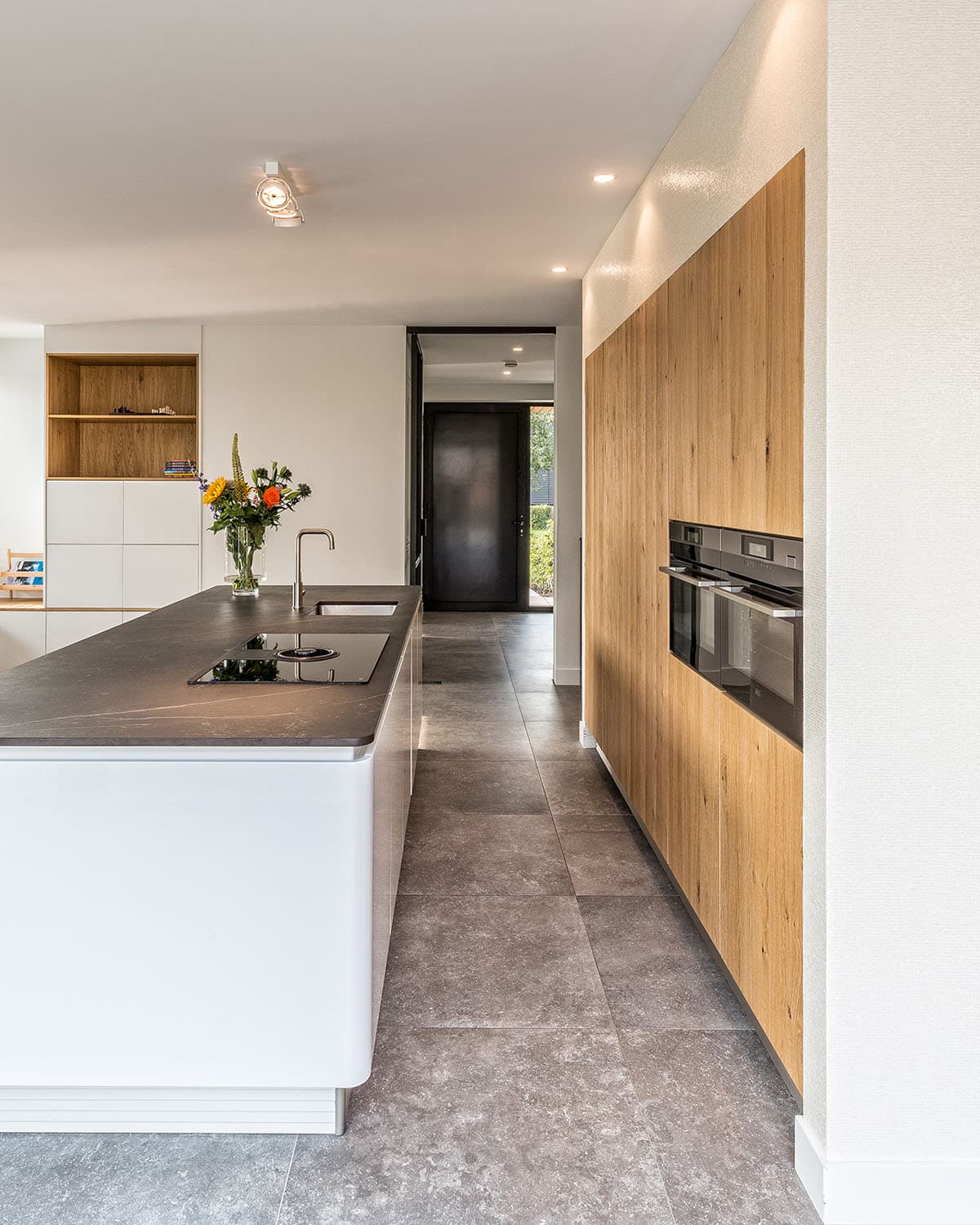 Detail van moderne keuken met houten kastenwand, wit kookeiland en stalen binnendeur