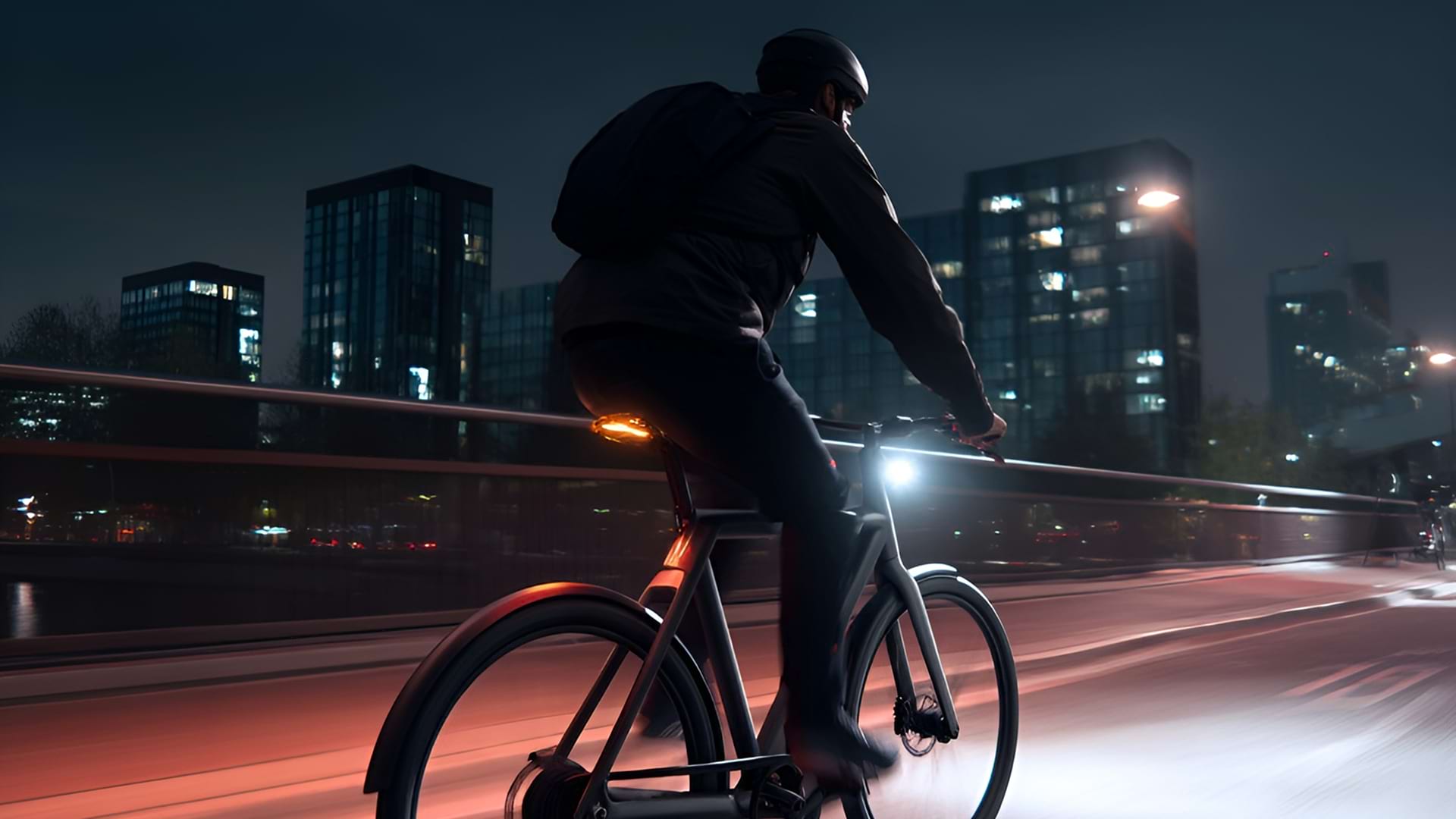 A person rides a bicycle at night on a city bridge, illuminated by streetlights and building lights. The scene conveys a sense of motion and urban adventure.