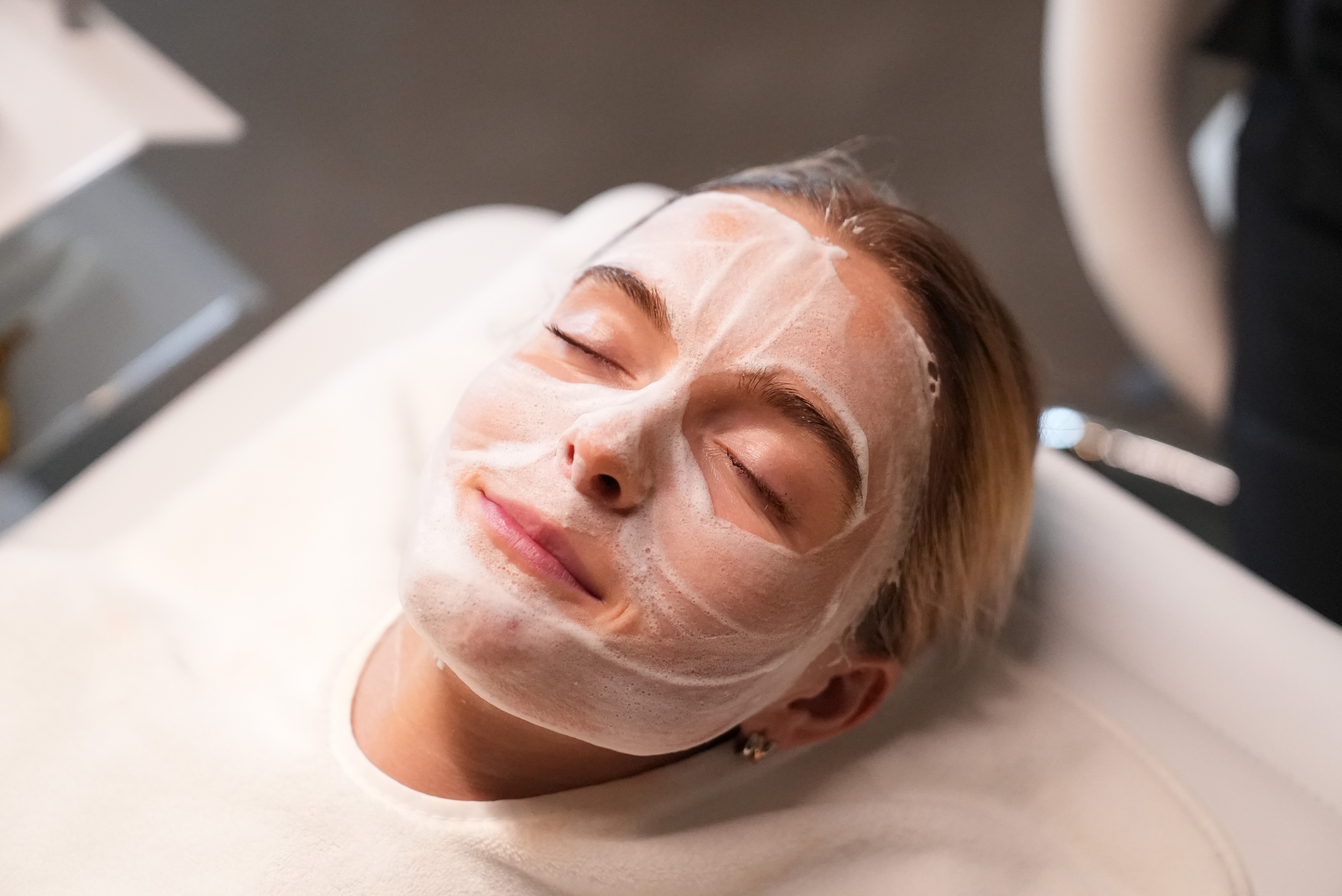 A person lying on a massage table, their face covered with a towel, bathed in warm golden light. The setting exudes relaxation and comfort.