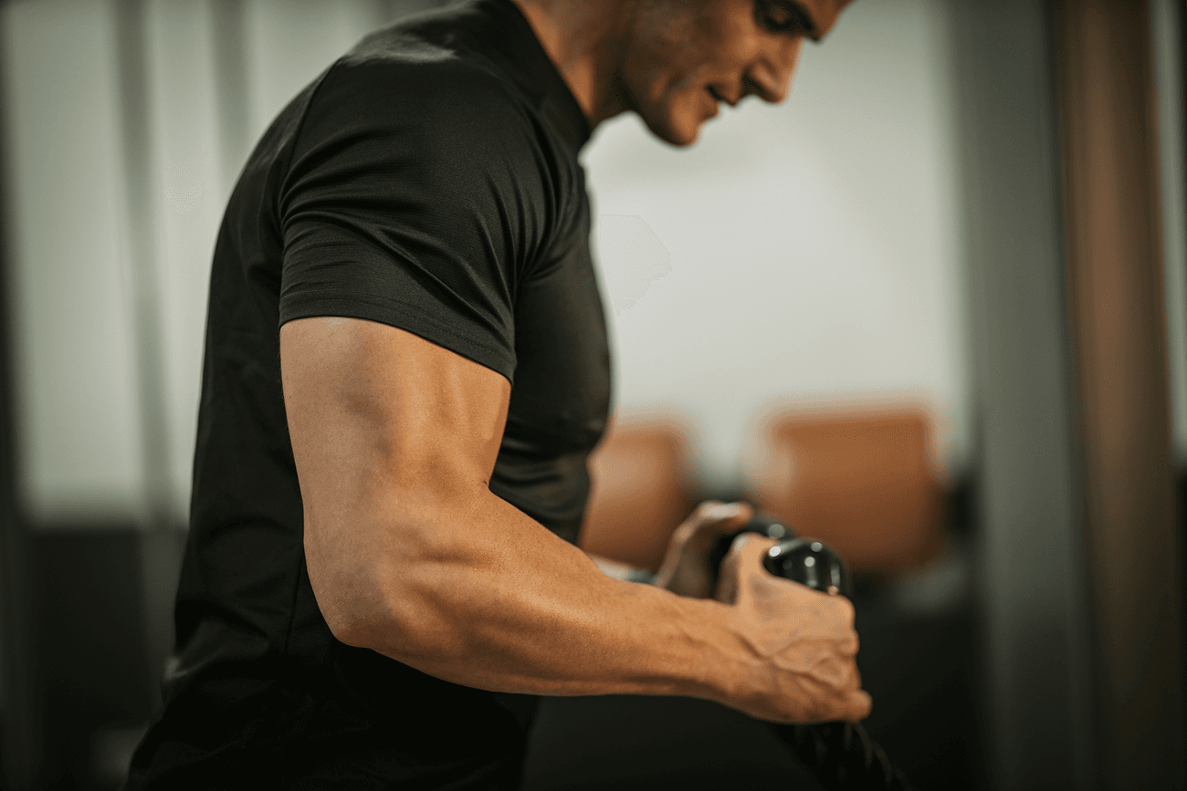 Close-up of a man’s flexed arm as he lifts a weight in a gym.