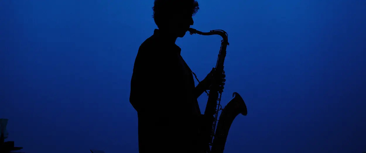 Guy playing sax as a silhouette in front of a blue screen