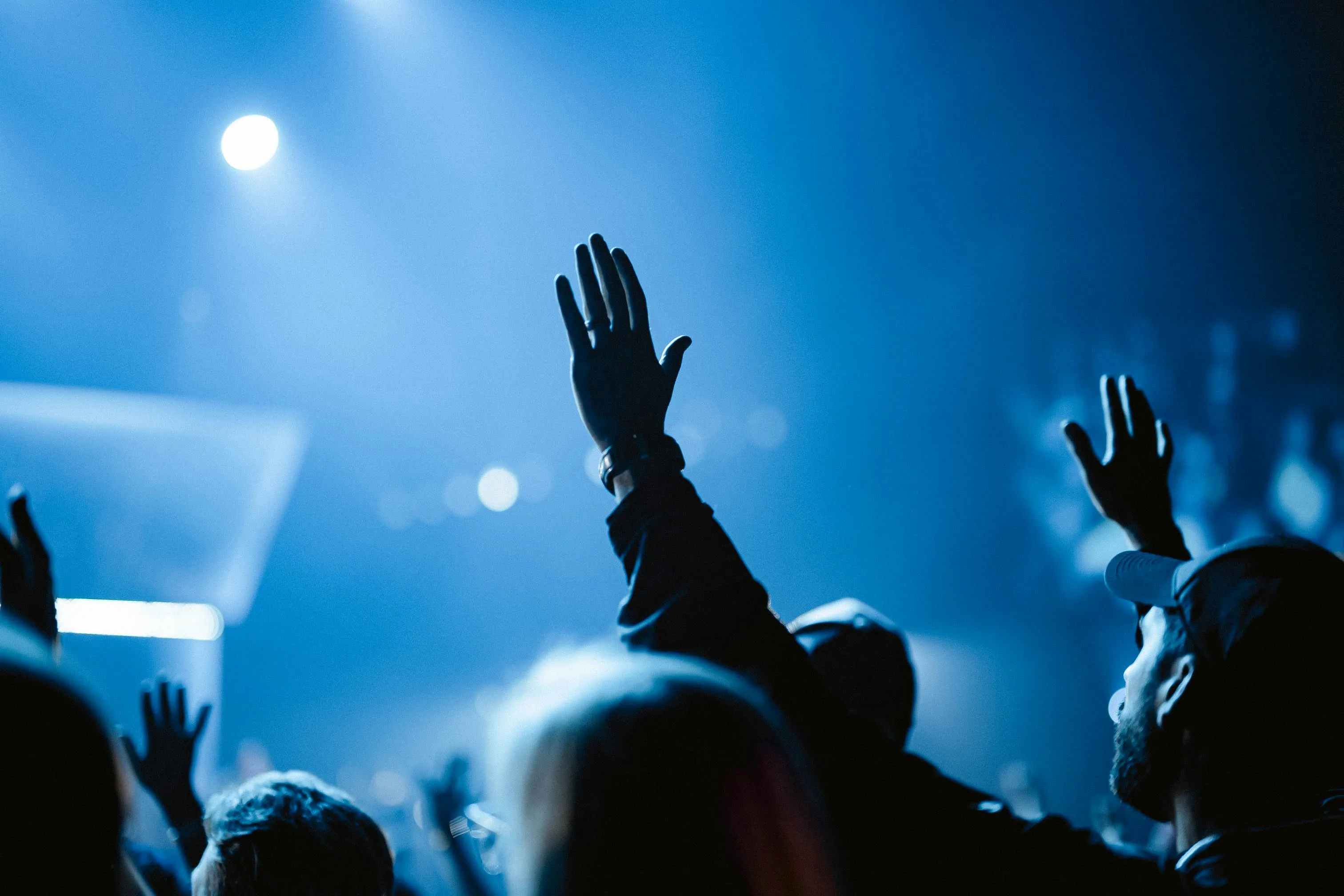 People with hands raised during a Sunday gathering, lit by blue stage light