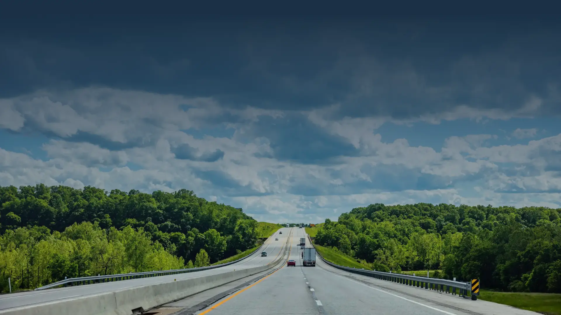 Open highway surrounded by green trees under a partly cloudy sky, representing GIA Group, LLC’s commitment to guiding truckers with clear answers and reliable insurance support.