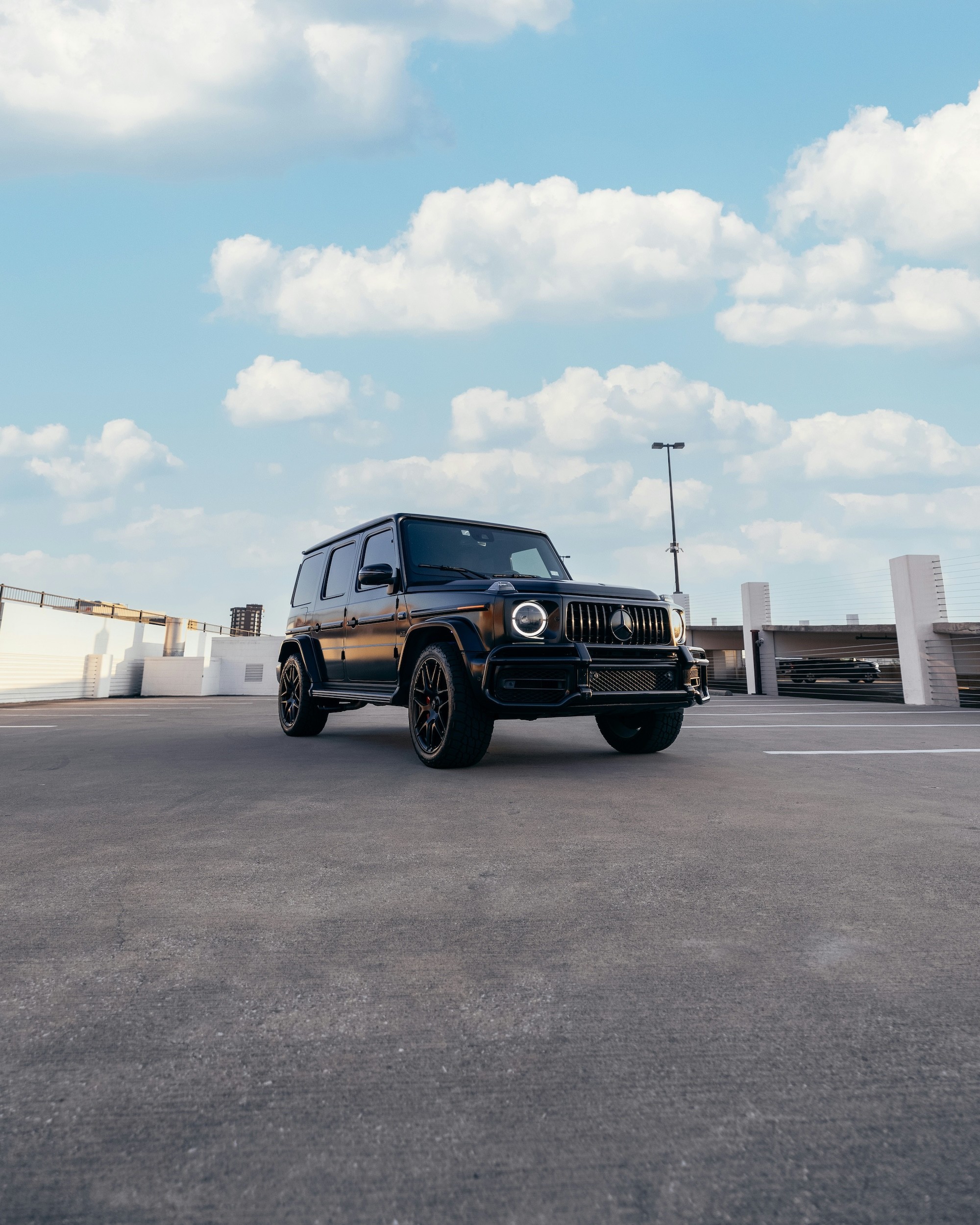 A black luxury SUV is parked on a rooftop parking lot under a bright, partly cloudy sky.