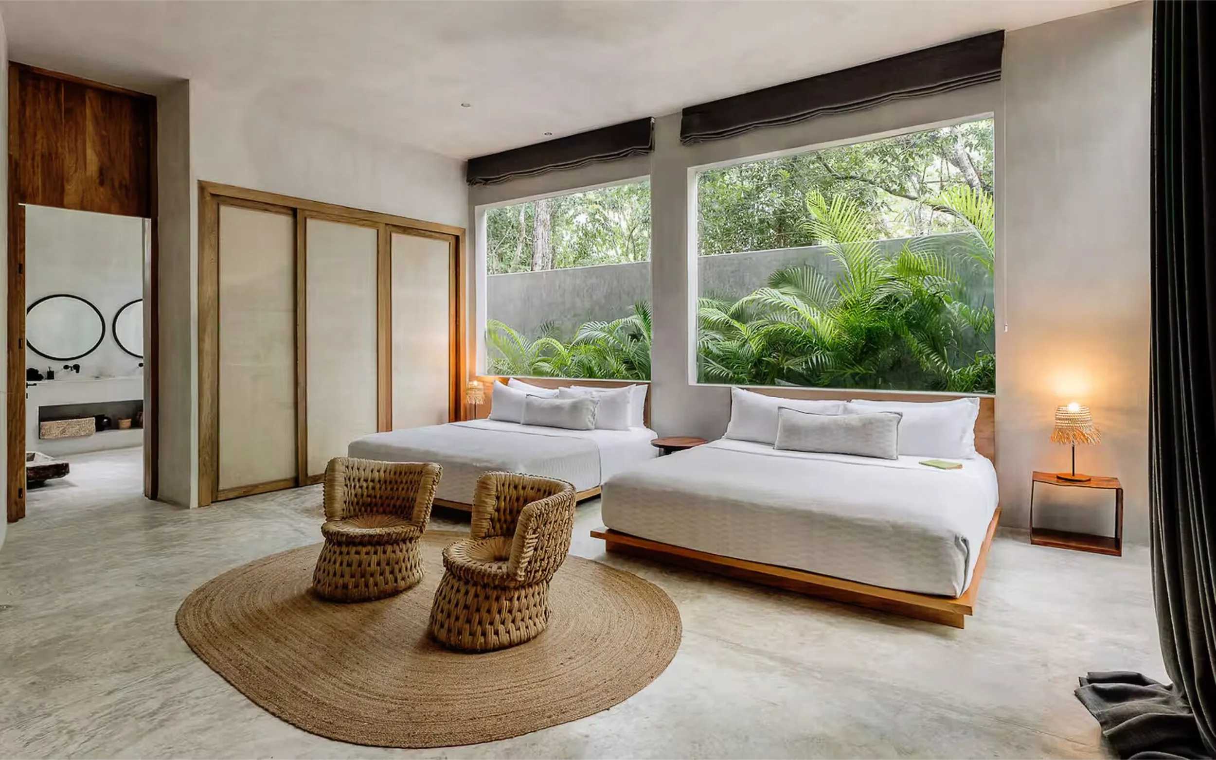 Serene double bedroom featuring large windows facing a green wall, neutral tones, and woven furniture.