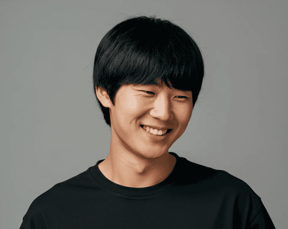 Smiling young man in a black T-shirt against a neutral gray background.