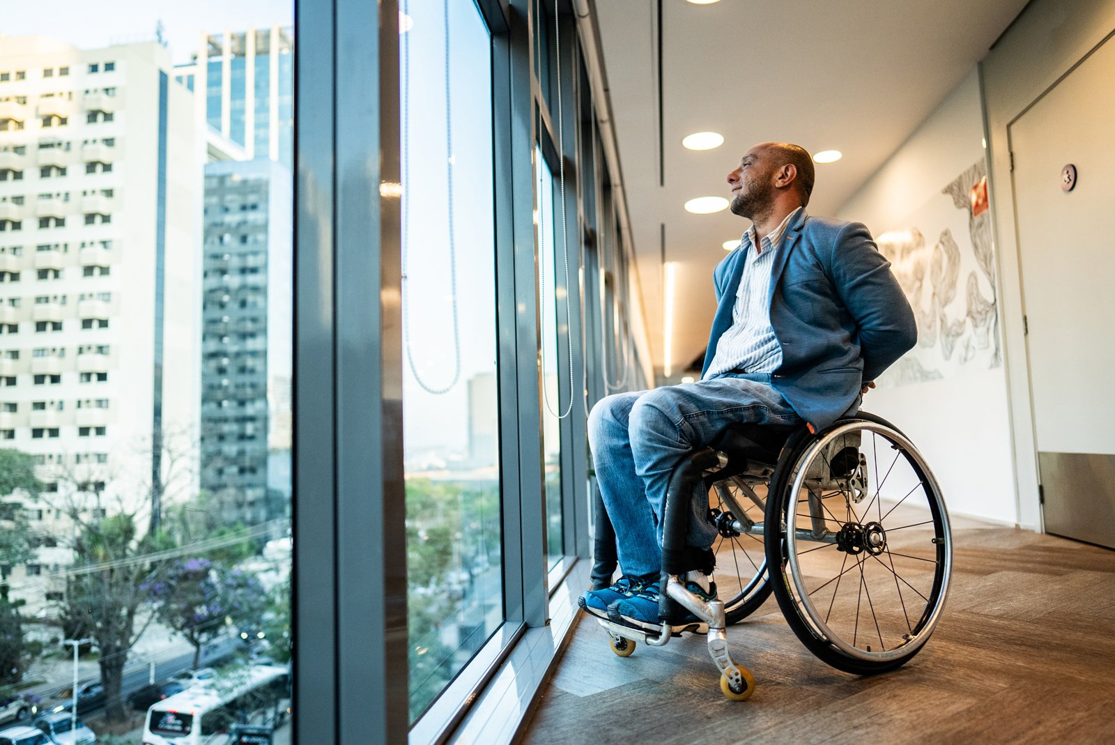 Man in a manual wheelchair looking out a tall window