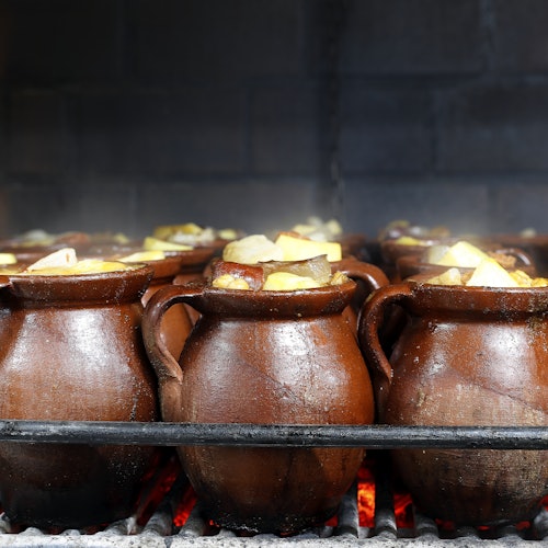 幾個褐色陶土鍋裡裝滿了塊狀的蔬菜,正在炭火下的烤架上烹煮,紅熱的煤炭可見於下方。
