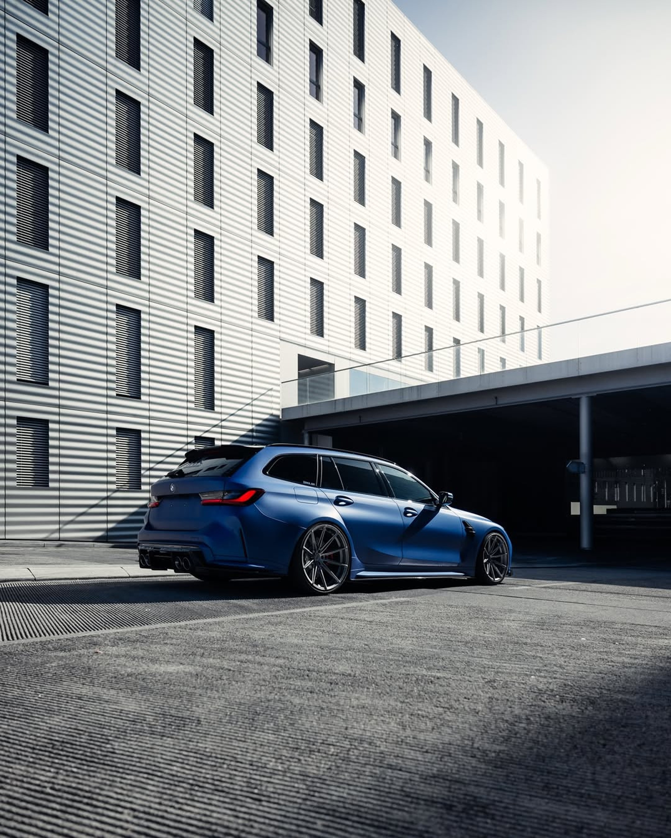 BMW M3 Touring bleue mate photographiée dans un environnement urbain moderne